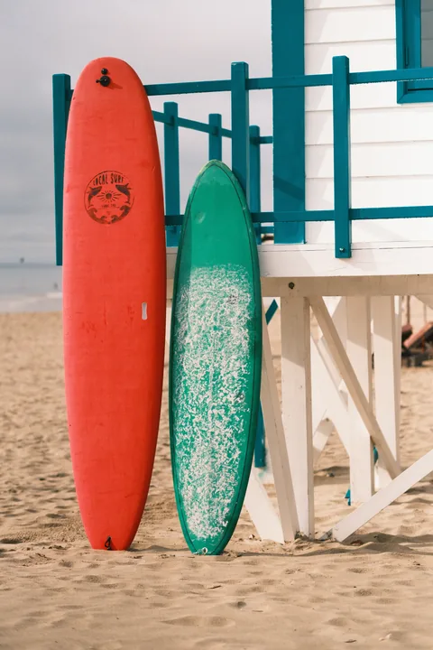 Red and green surfboards rest beside a turquoise beach hut.