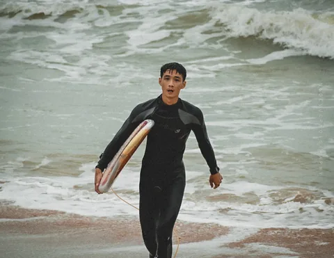 Yuki carries a surfboard out of the shore break.