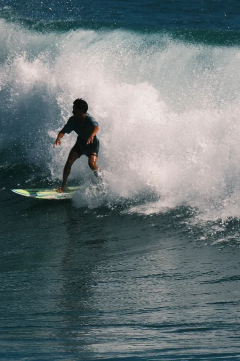 A surfer holds a steady line ahead of breaking spray on a surf trip.